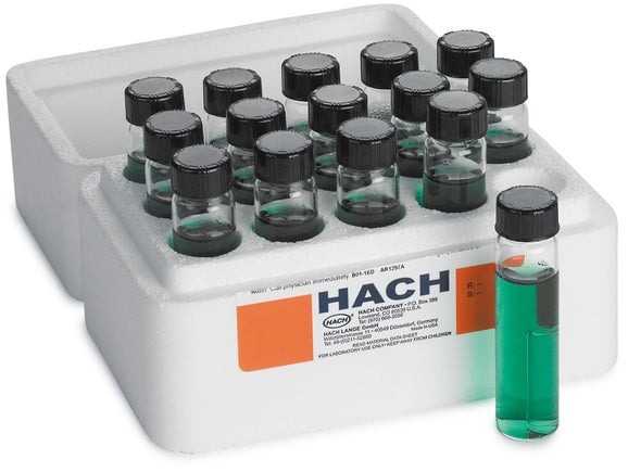 Tray of small glass vials with green liquid and black caps in a white foam rack, one vial standing outside the tray